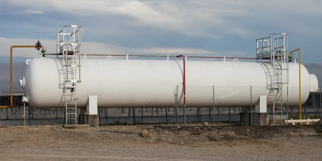 Deux professionnels en tenue de sécurité installant une citerne de gaz propane cylindrique blanche avec du matériel de manutention dans la zone extérieure d'un établissement professionnel